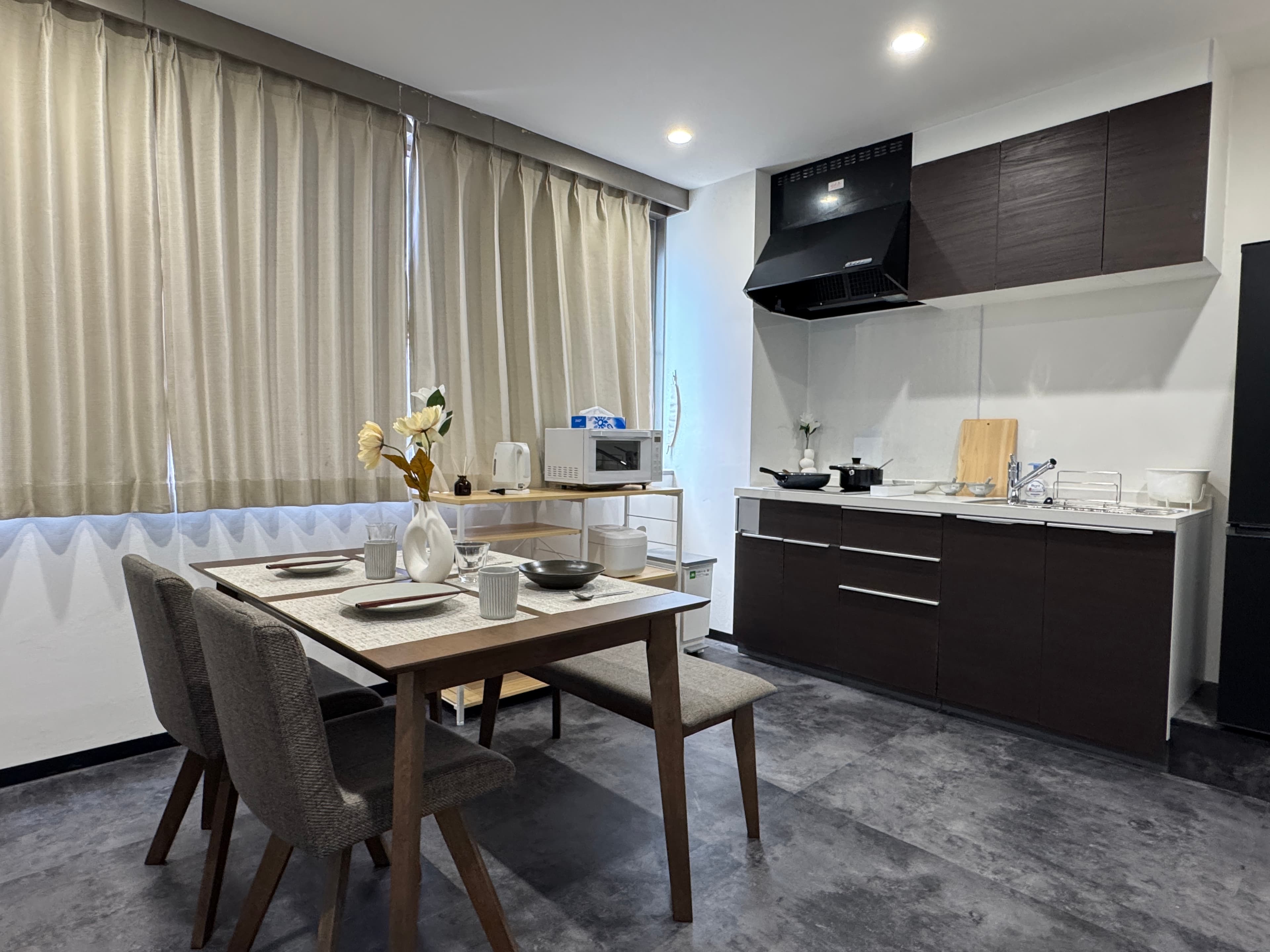 Wooden dining table with chairs and a bench next to a kitchen with dark brown cabinets.