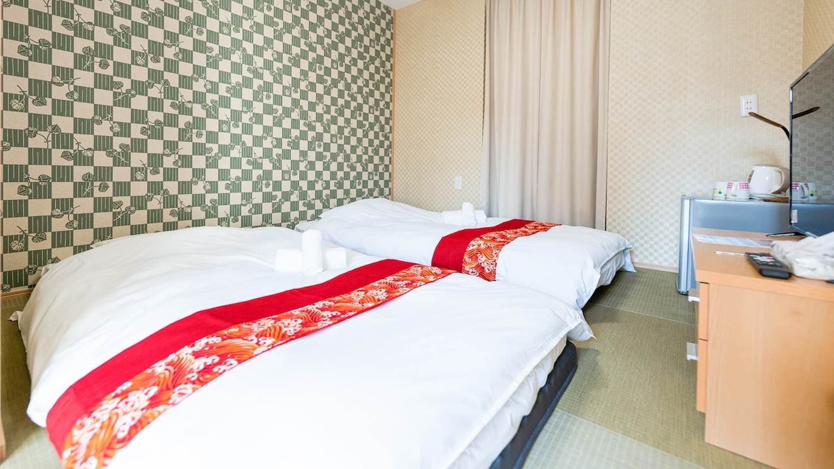 Japanese-style bedroom with two twin beds, tatami flooring, green patterned wallpaper, and a TV stand.