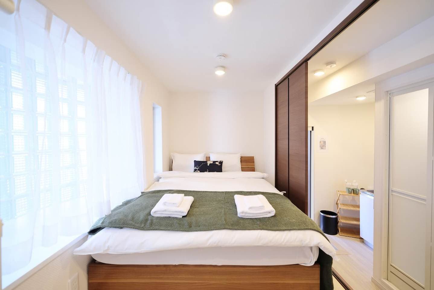 Compact bedroom with a double bed, green throw blanket, and sheer white curtains.