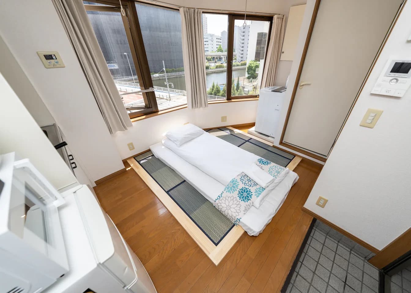 Japanese futon bed on tatami mats in a compact room with large windows overlooking a canal.