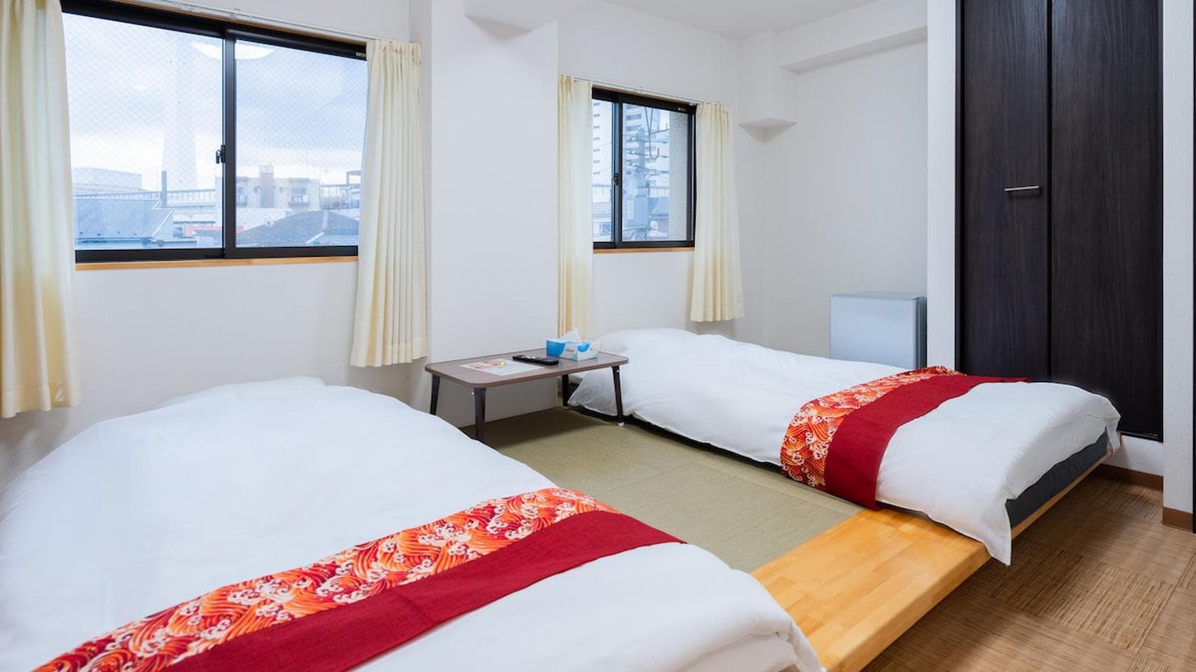 Two single beds with red patterned runners on a raised tatami floor in a bright bedroom.