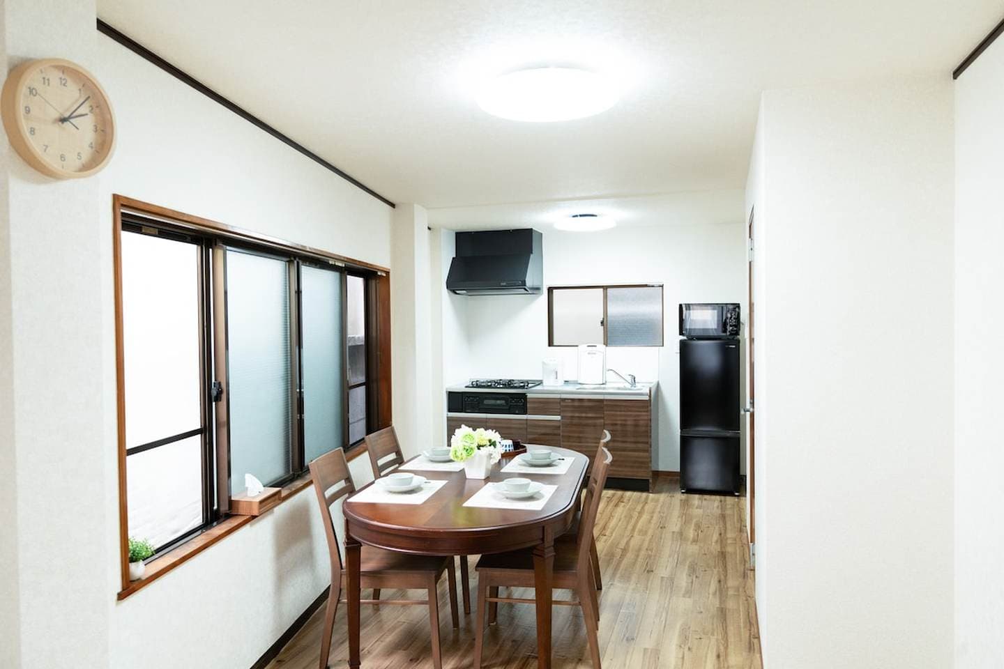 Wooden dining table and chairs set for a meal next to a kitchen with a black refrigerator.
