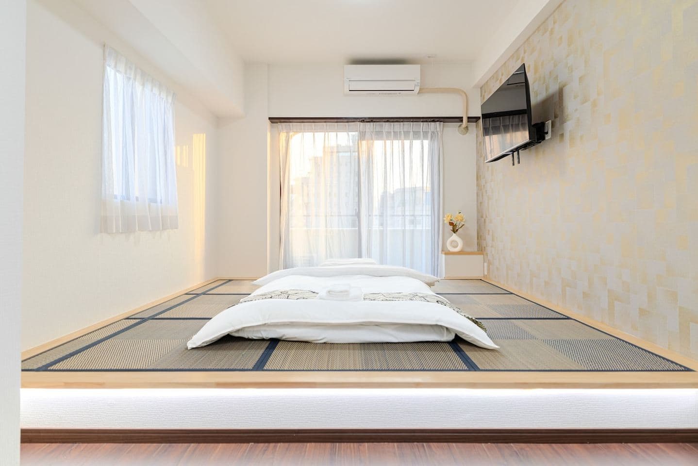 Japanese-style bedroom featuring a white futon on a raised tatami mat platform with a wall-mounted TV.