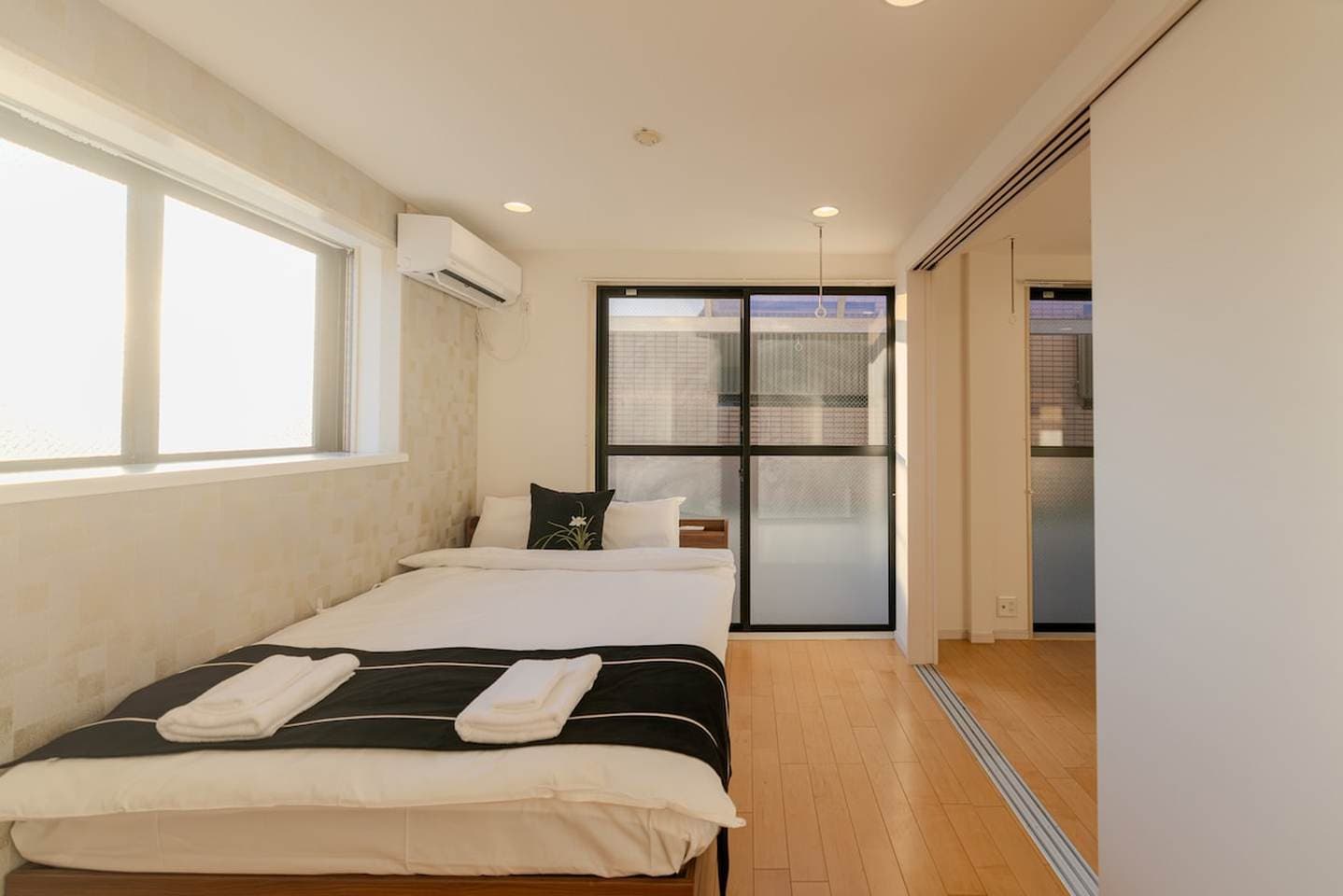Bright bedroom with a double bed, white linens, hardwood flooring, and sliding glass doors.