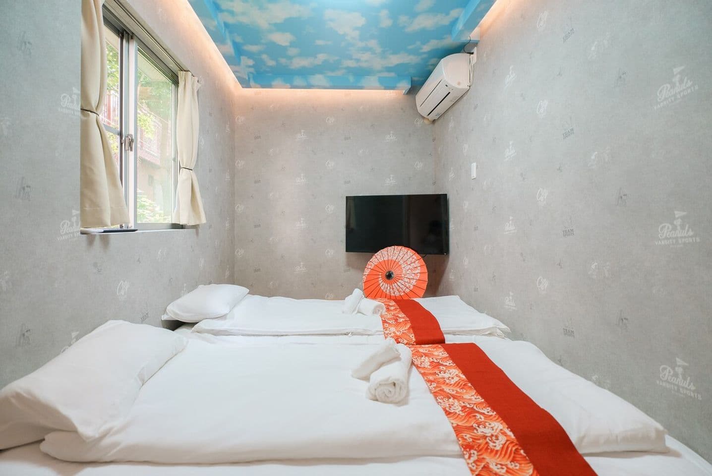 Bedroom with two floor beds, a sky-patterned ceiling, wall-mounted TV, and a decorative Japanese umbrella.