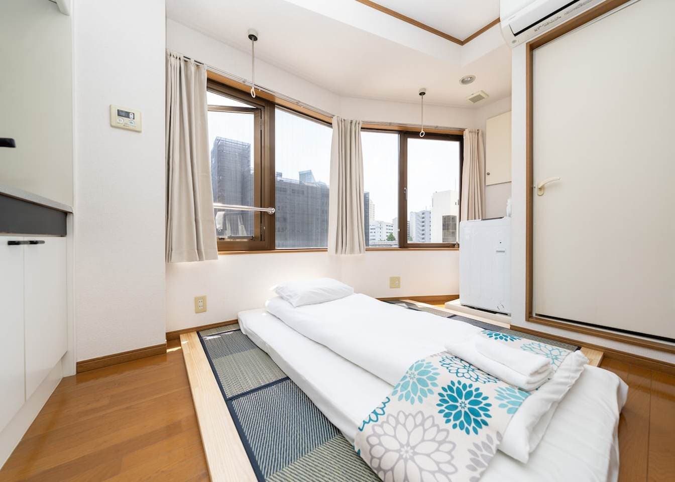 Japanese futon bed on tatami mats in a bright room with large windows.