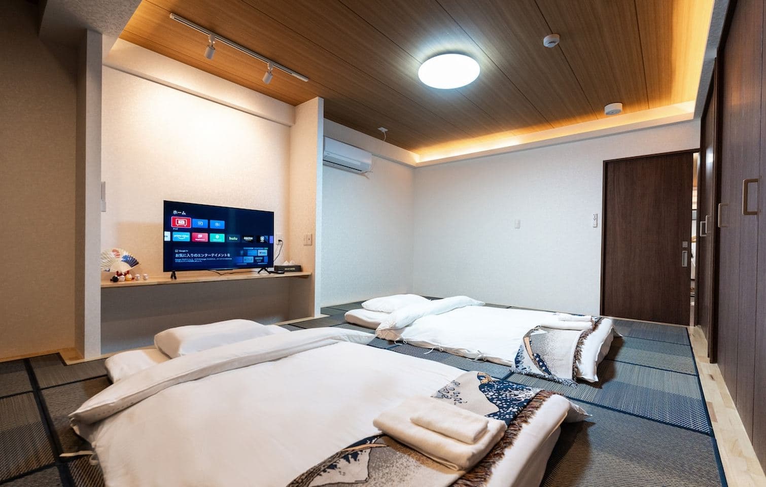 Modern Japanese-style bedroom with two futons on tatami mats and a television.