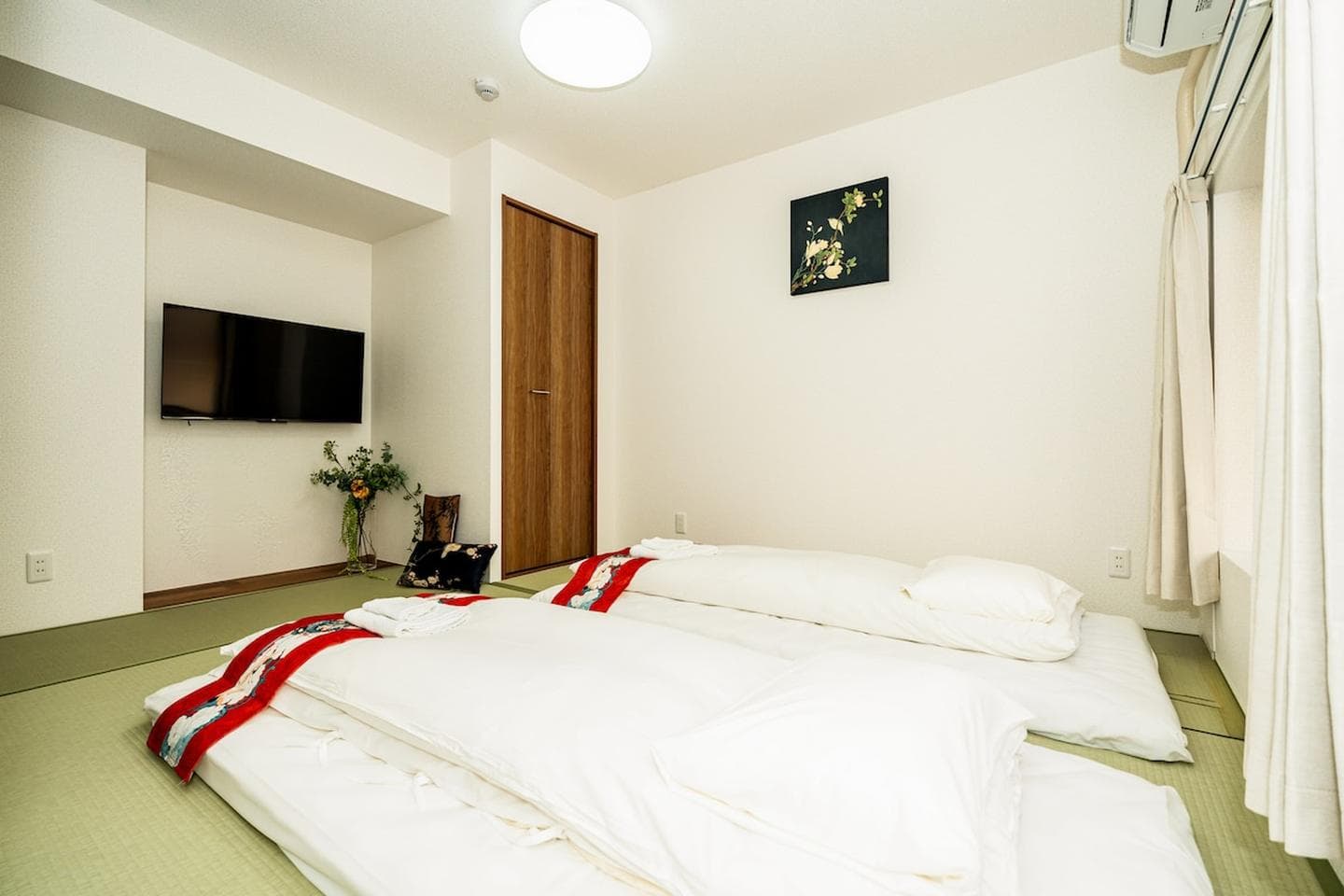 Japanese-style bedroom with two white futons on tatami mats and a wall-mounted TV.
