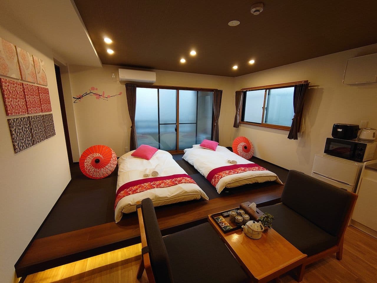 Japanese-style bedroom with two futon beds on a raised platform, low chairs, and traditional red paper umbrellas.