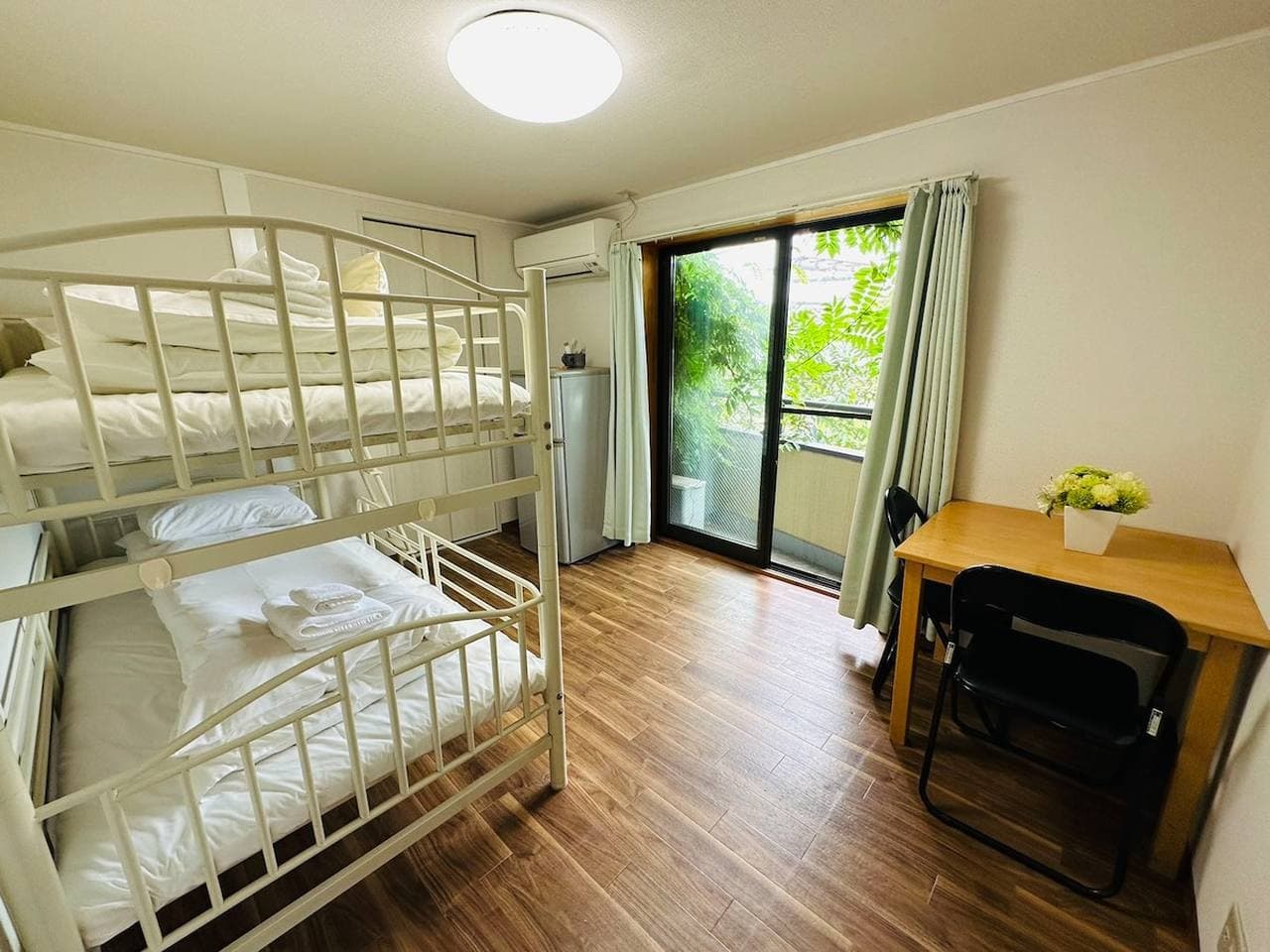 Bedroom with a white metal bunk bed, wooden desk, and sliding glass doors leading to a balcony.