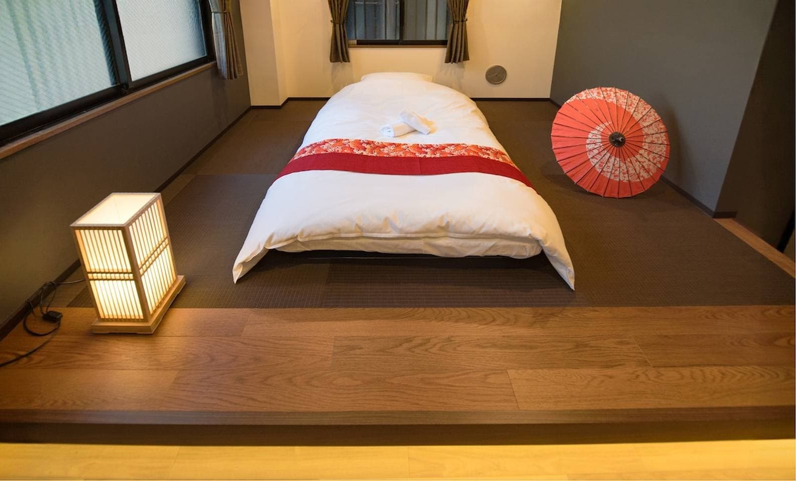 Japanese-style bedroom with a white futon on a raised tatami floor, a paper lantern, and a red umbrella.