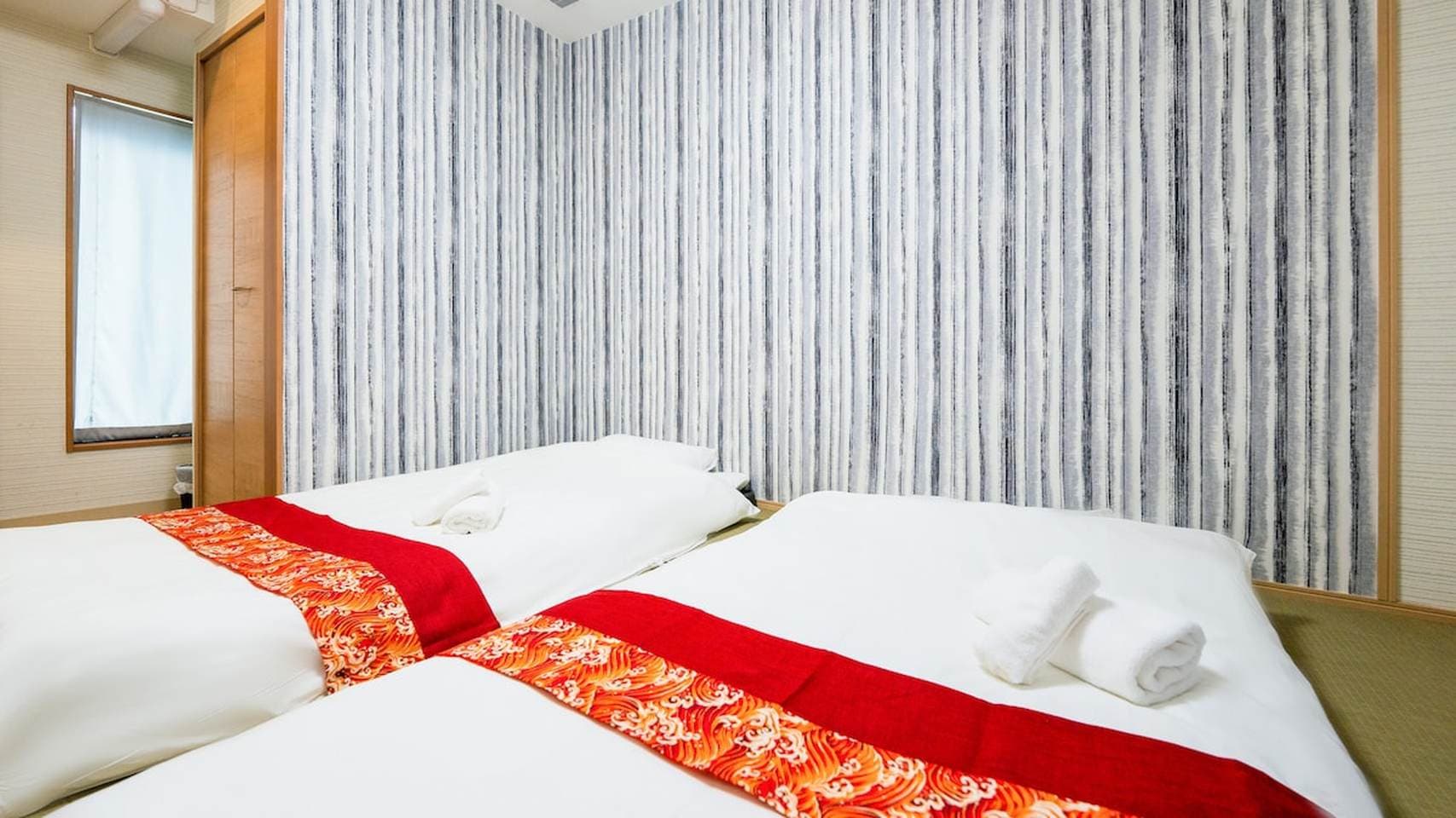 Two low beds with white linens and red patterned runners against a blue and white striped accent wall.