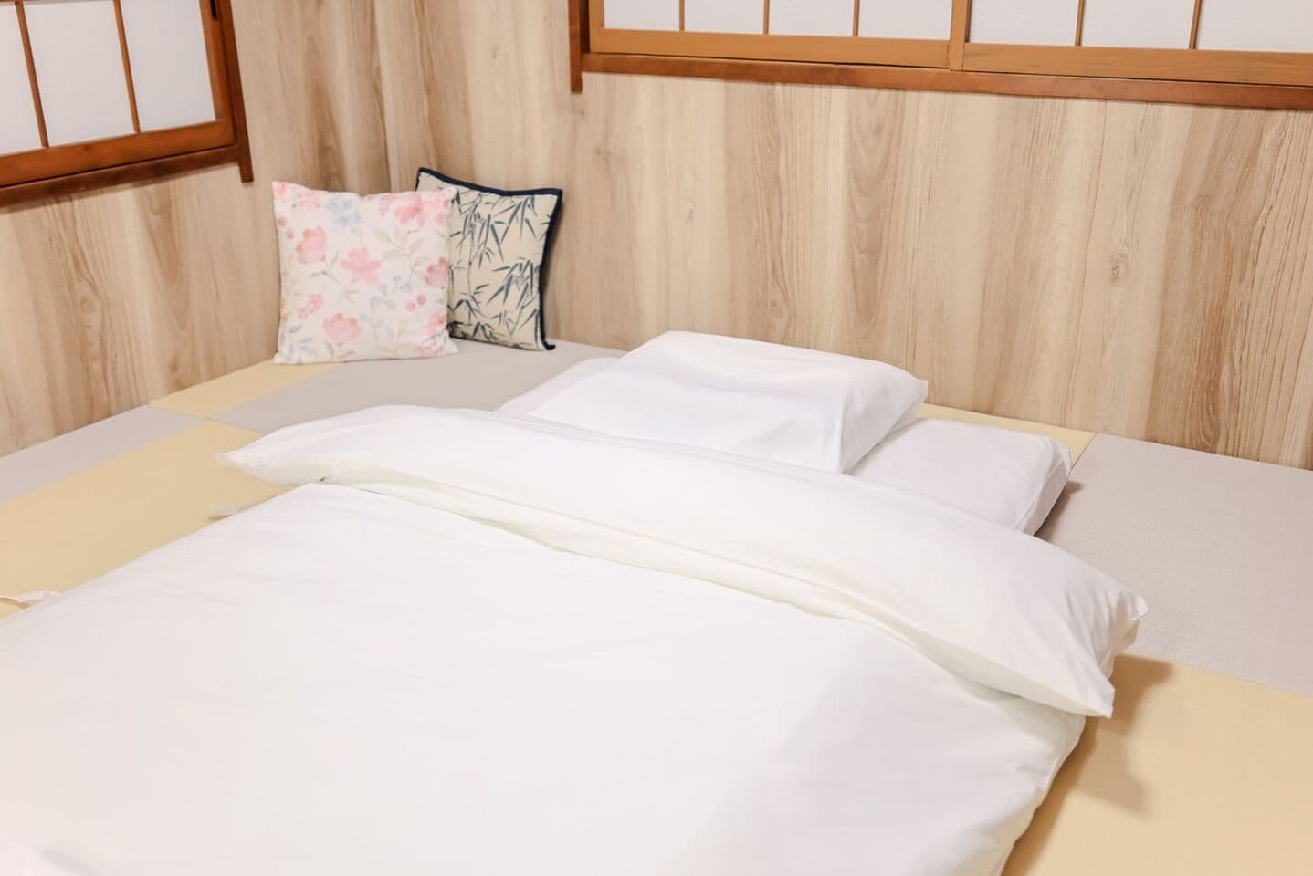 Traditional Japanese futon bed with white linens on tatami mats in a wood-paneled room.