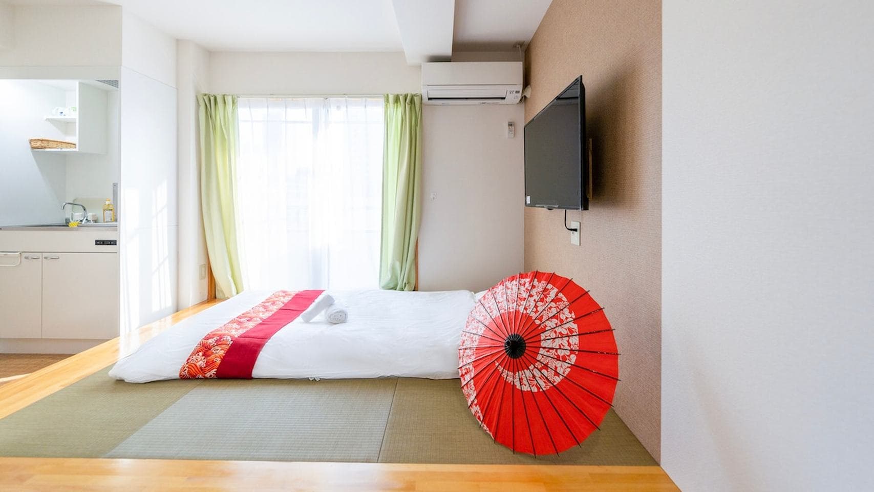 Japanese-style bedroom with a futon on tatami mats, a red traditional umbrella, and a wall-mounted TV.