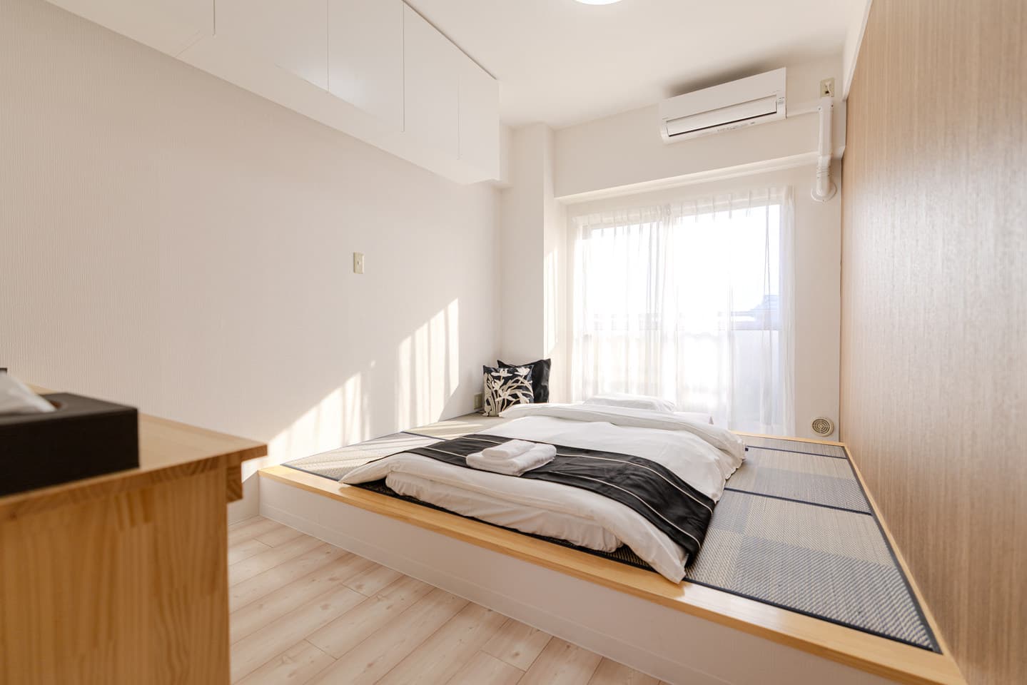 Futon bed on a raised tatami mat platform in a bright bedroom with sheer curtains.