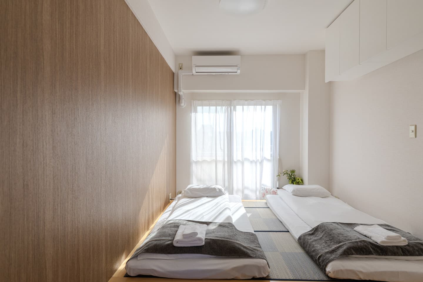 Two futons on a tatami platform in a bedroom with a wooden accent wall and bright window.