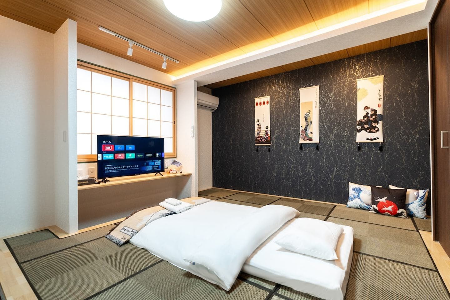 Japanese-style bedroom with tatami mats, a futon bed, a television, and decorative wall scrolls.