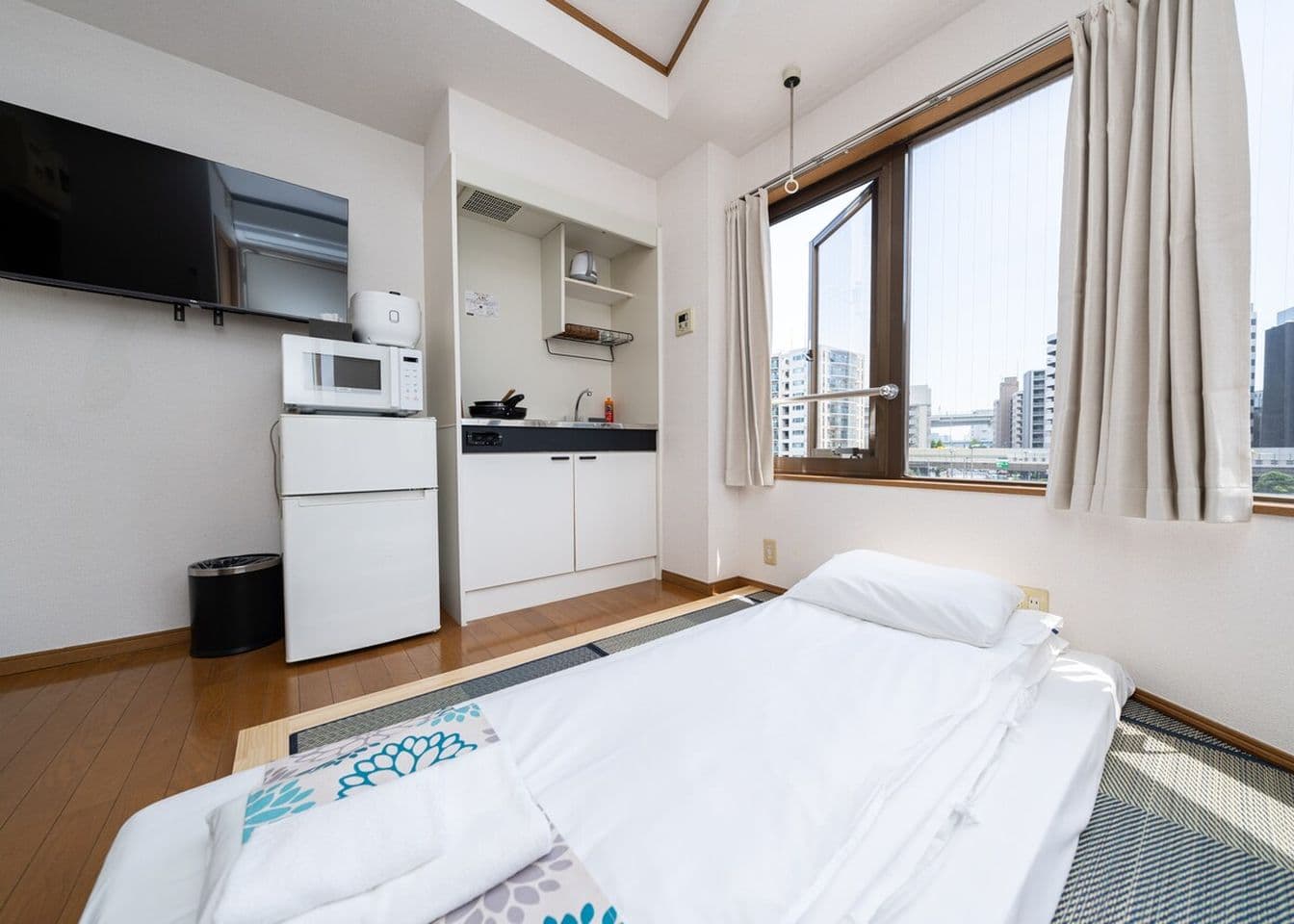 Compact studio apartment with a futon bed, small kitchenette, refrigerator, and a window with city views.