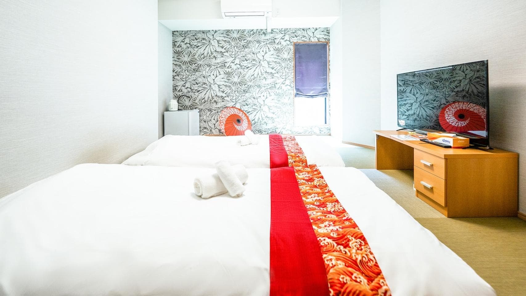 Bedroom with two beds featuring red patterned runners, a TV stand, and decorative wallpaper.