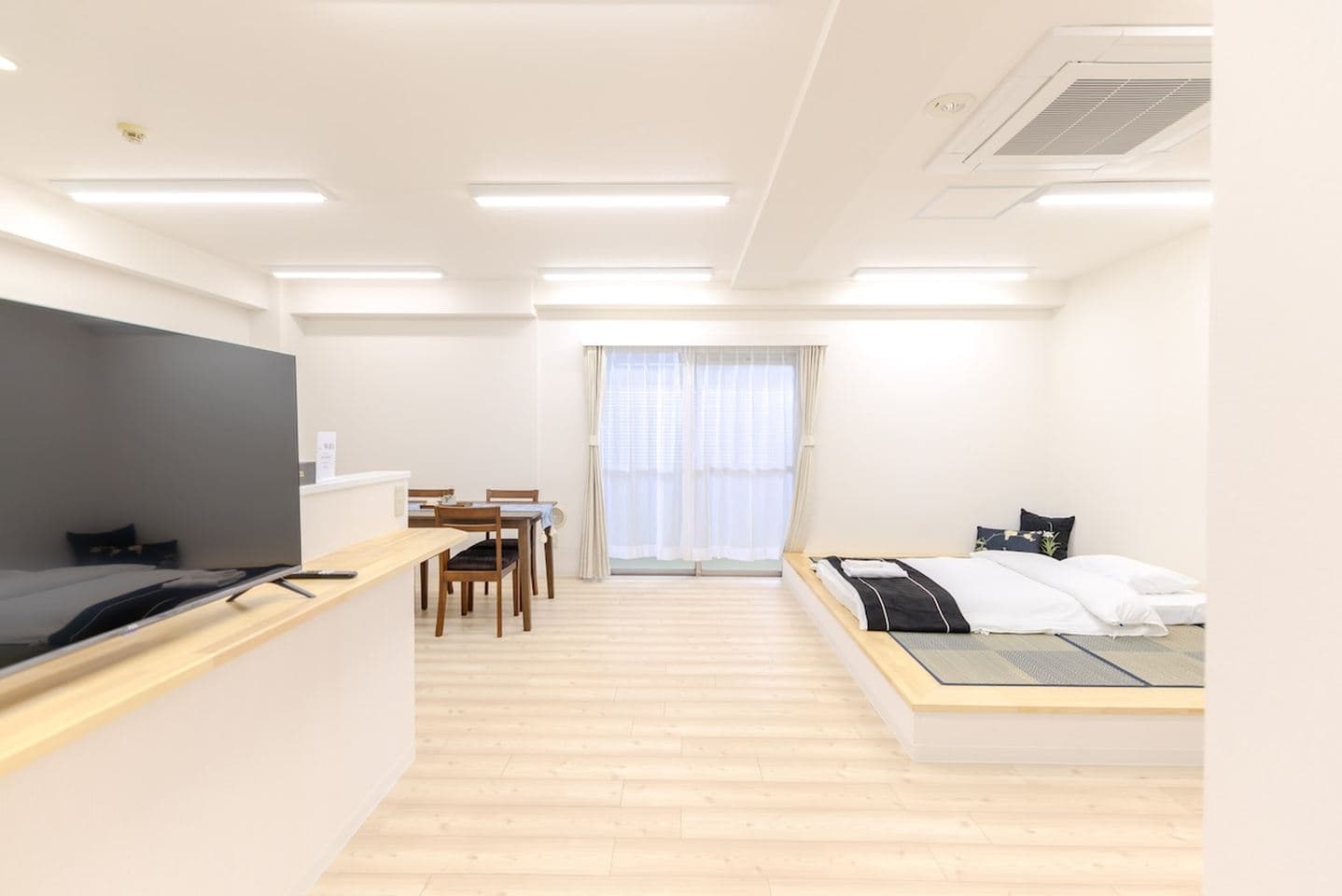 Open-plan studio apartment with a raised tatami bed platform, dining table, and flat-screen TV.