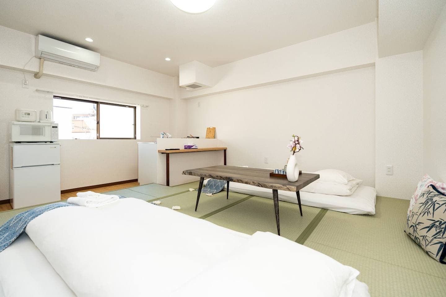Japanese-style room with tatami mats, futon bedding, a low wooden table, and a small refrigerator.