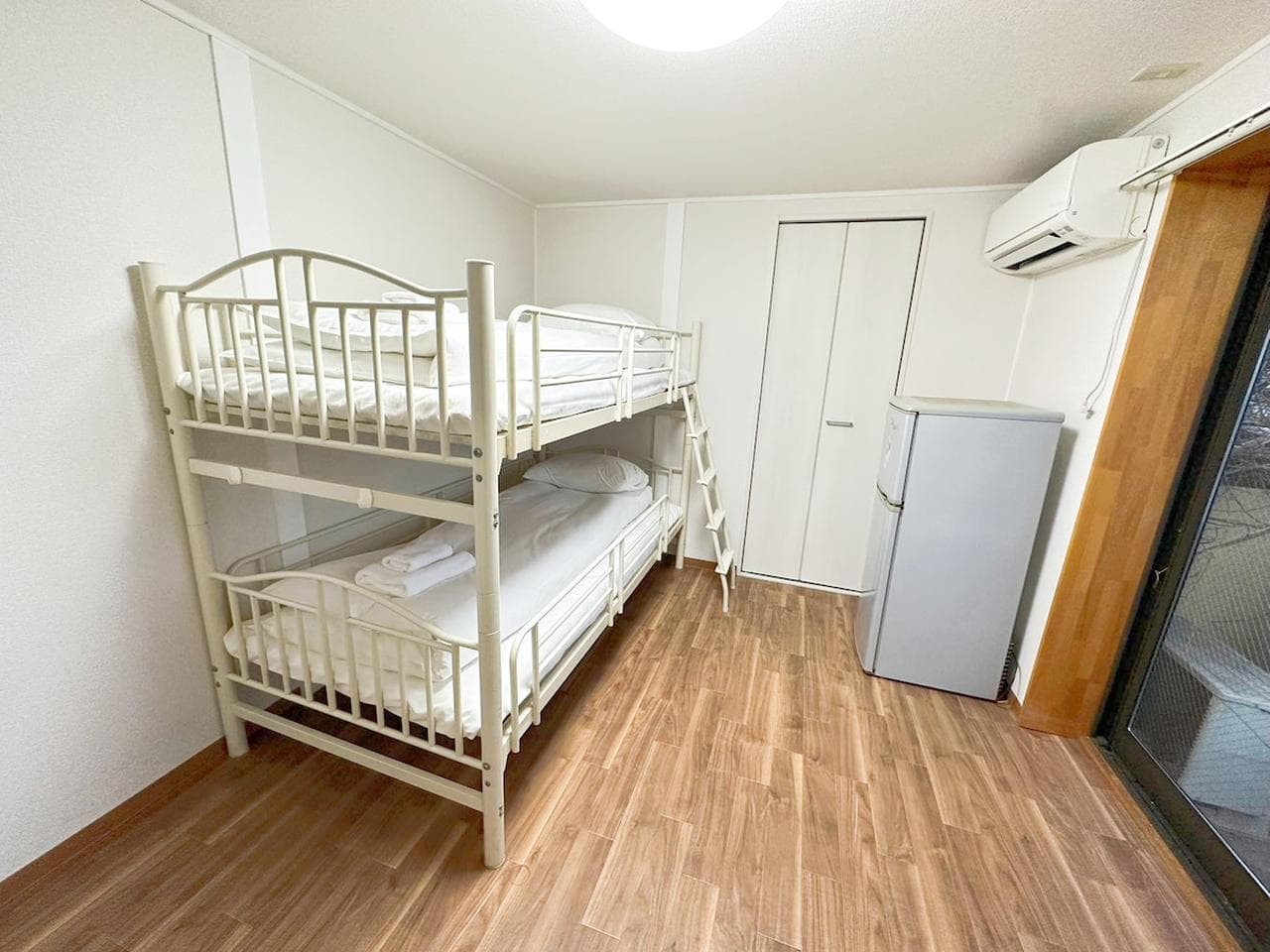 Bedroom with a white metal bunk bed, a small refrigerator, and wood-look flooring.