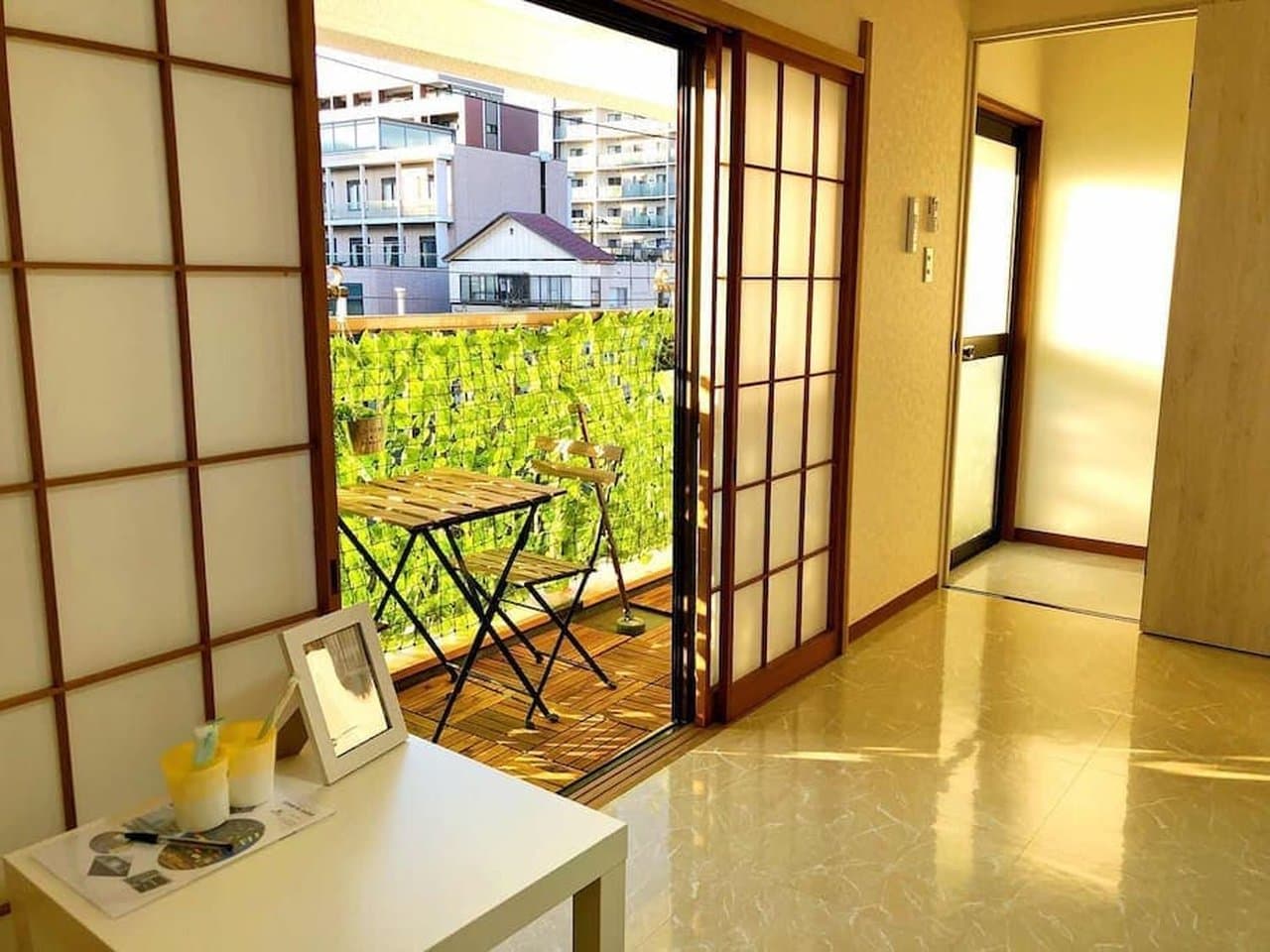 View of a sunny balcony with a wooden table and chairs through open shoji sliding doors.