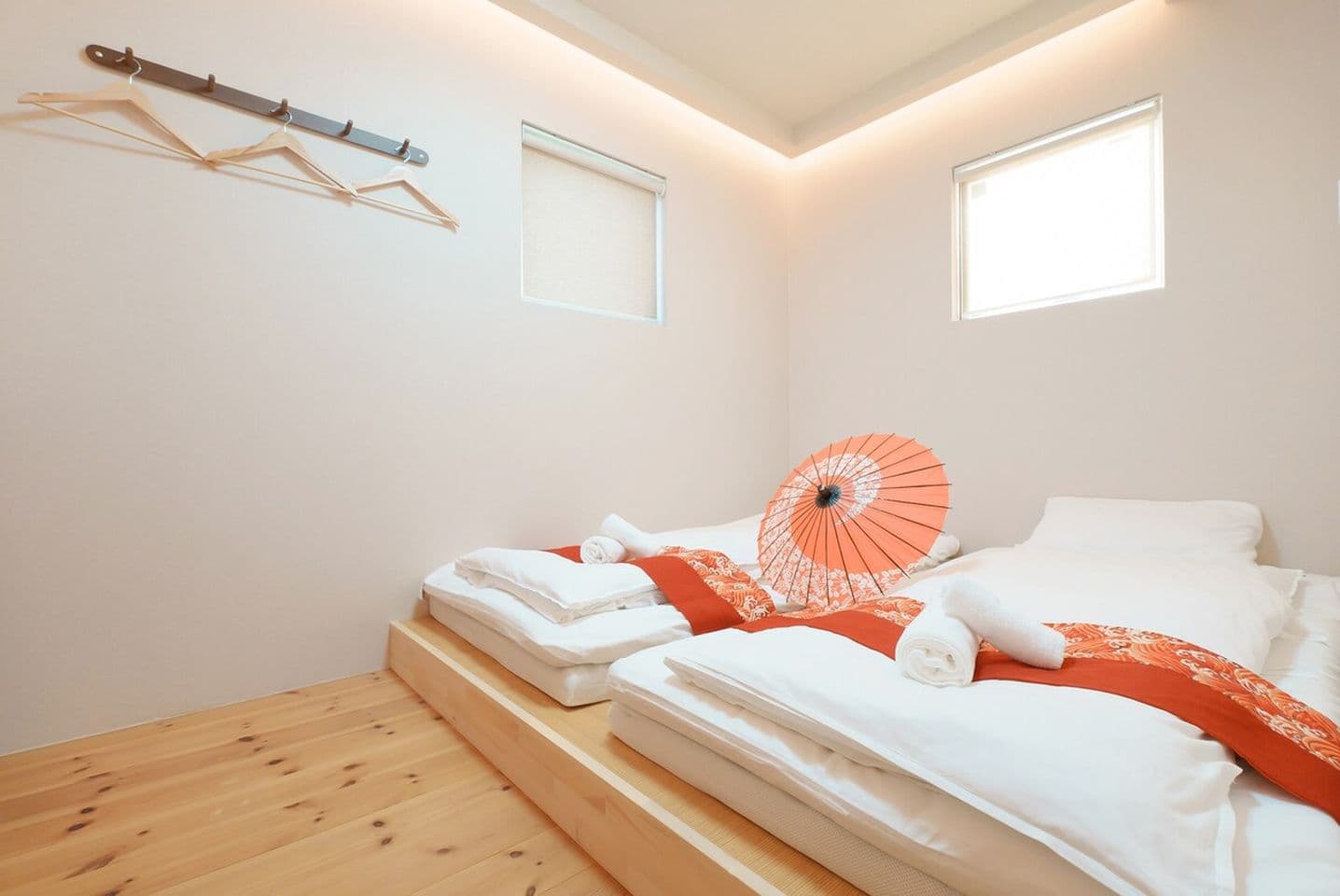 Two beds on a raised wooden platform with white linens, orange runners, and a traditional Japanese umbrella.