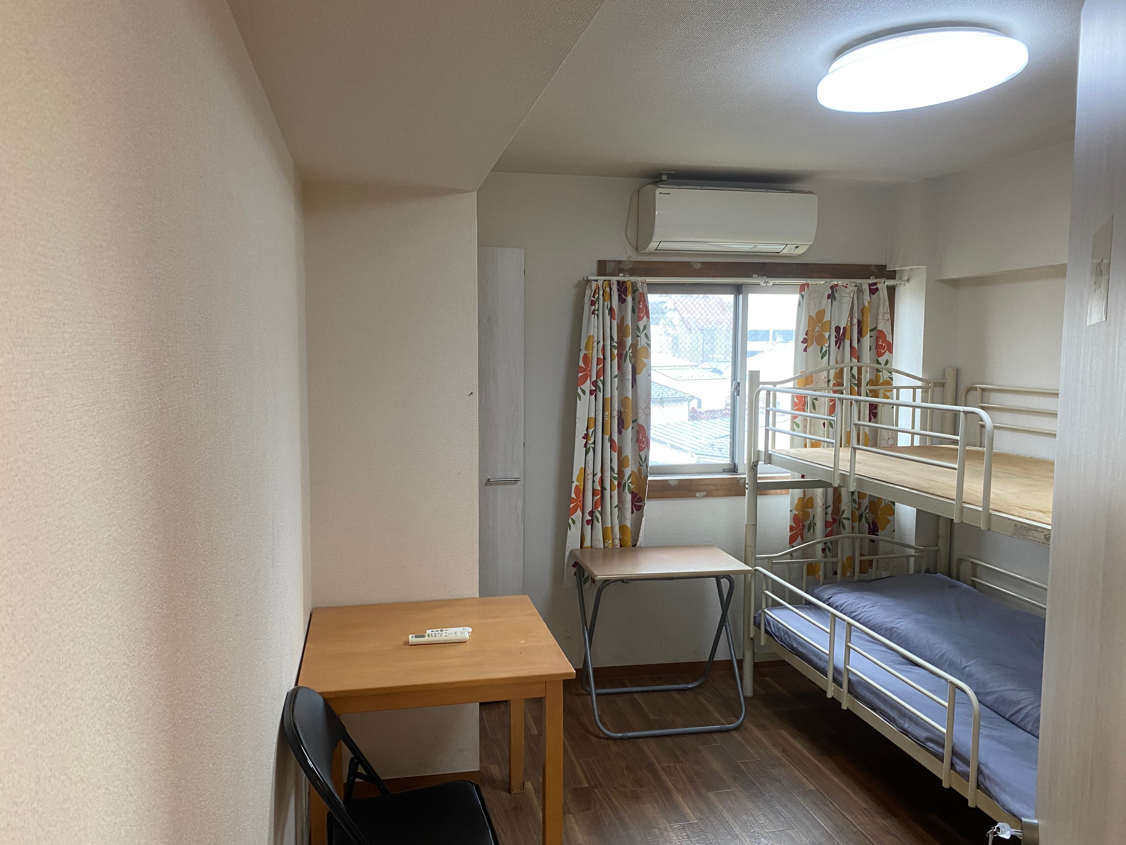 Compact bedroom featuring a metal bunk bed, two wooden desks, and floral curtains by the window.