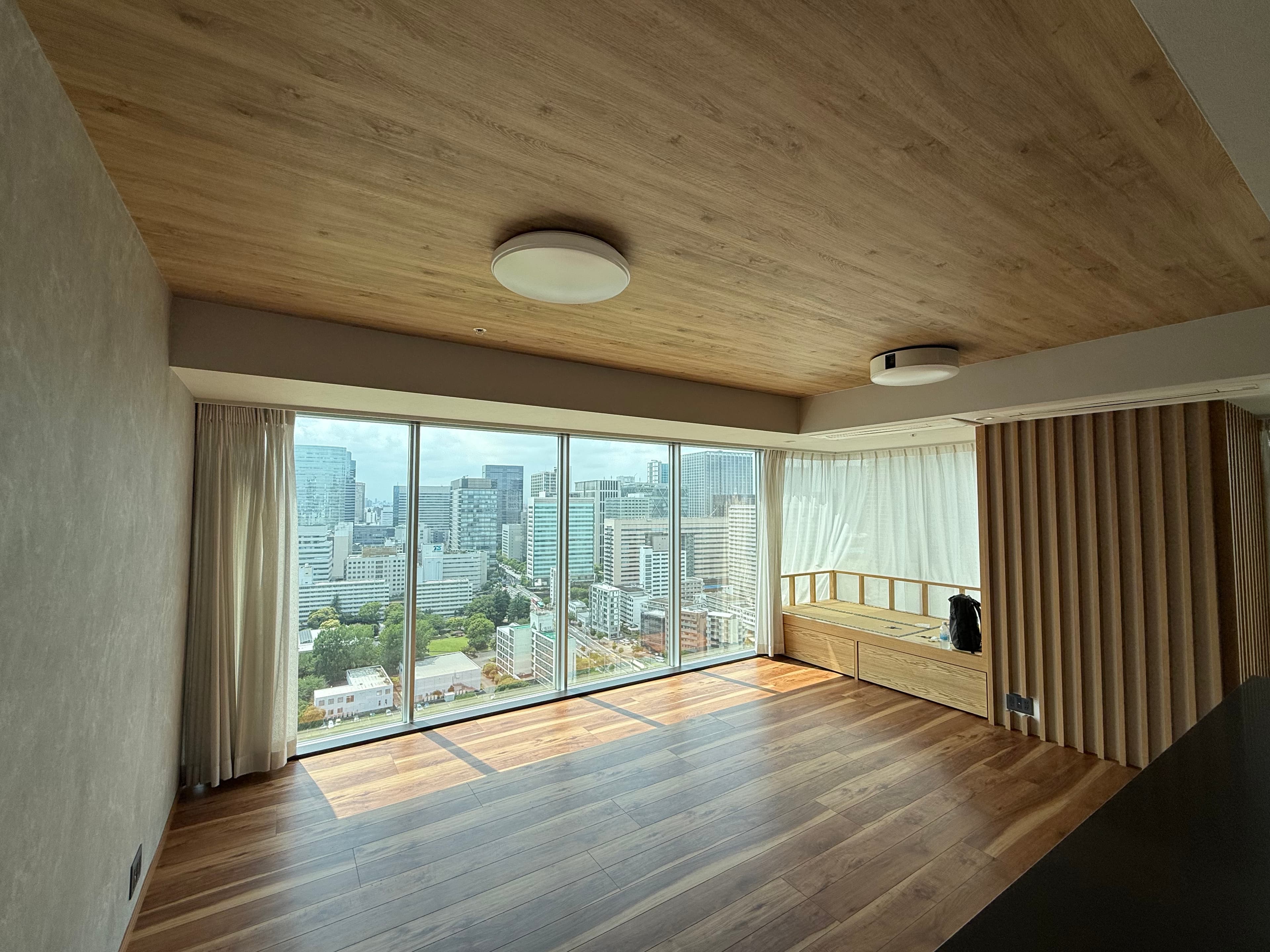 Empty modern room with wood floors, wood ceiling, and large windows overlooking a Tokyo city skyline.