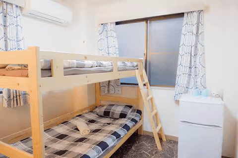 Bedroom with a wooden bunk bed, plaid bedding, and a small white refrigerator next to a window.