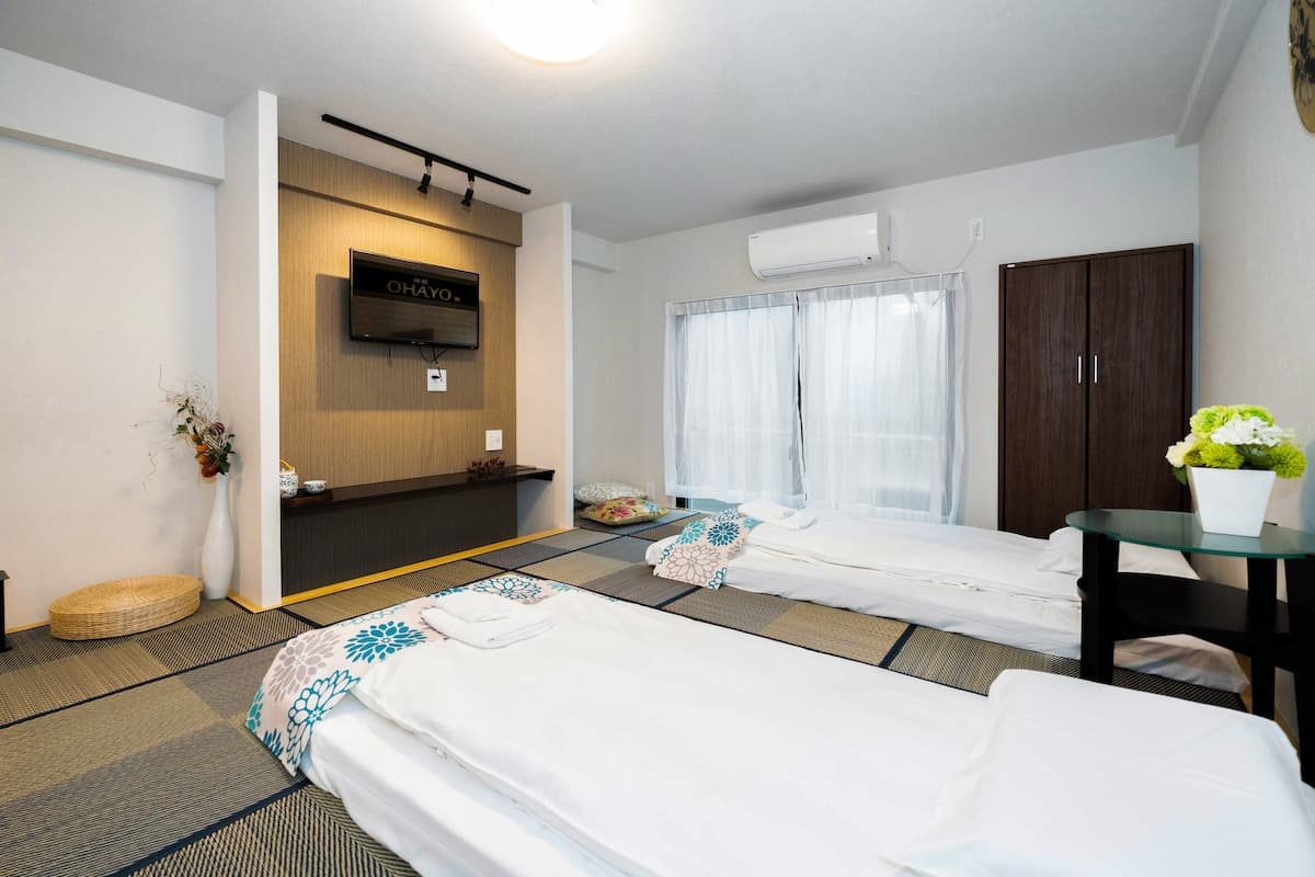 Japanese-style bedroom with two futons on tatami mats, a wall-mounted TV, and a wardrobe.