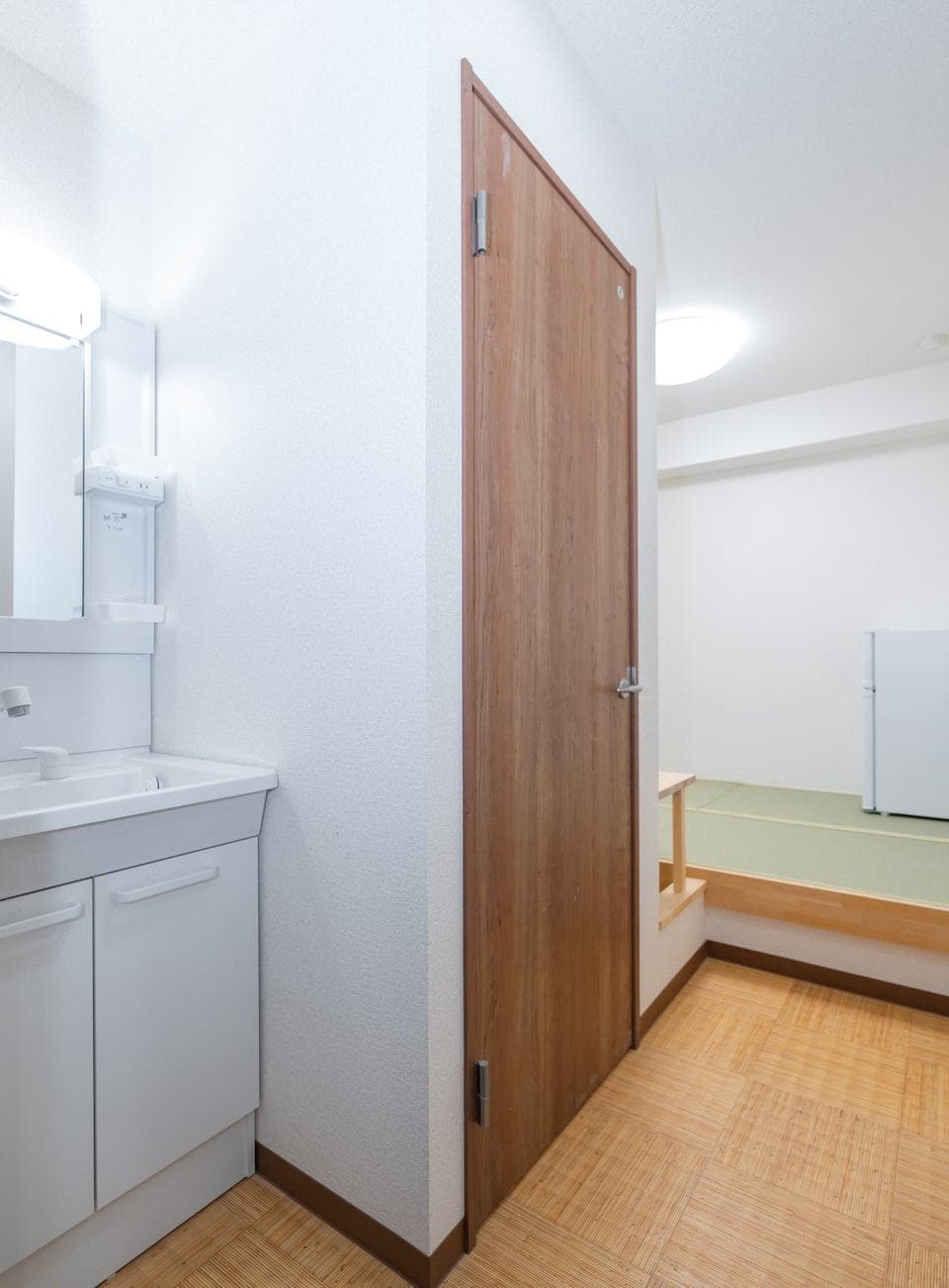 Compact bathroom sink vanity next to a wooden door with a tatami room visible in the background.