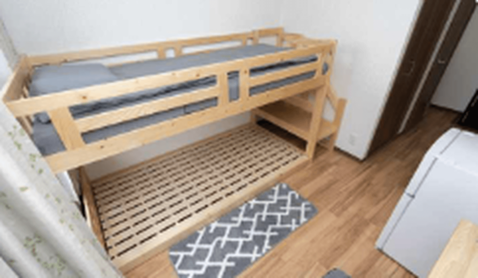 Wooden bunk bed with grey bedding on the top bunk in a room with hardwood floors.
