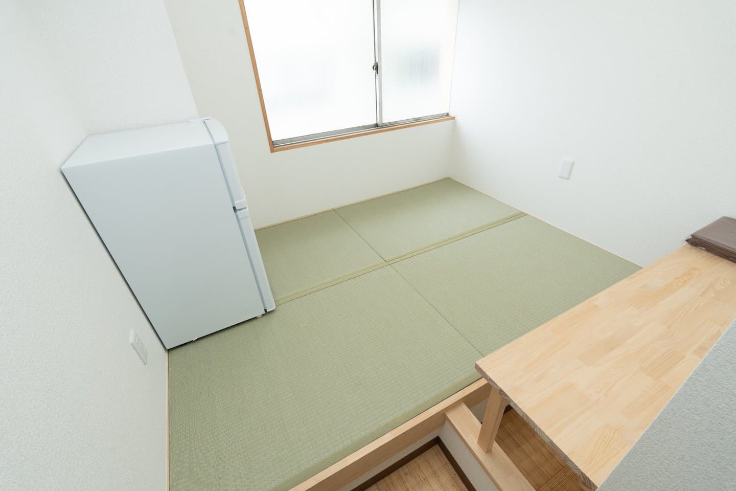 Japanese-style room with green tatami mats, a small white refrigerator, and a wooden desk.