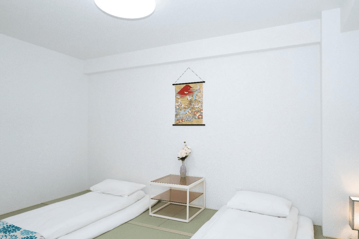 Two white futons on tatami mats in a minimalist bedroom with a small side table and wall hanging.