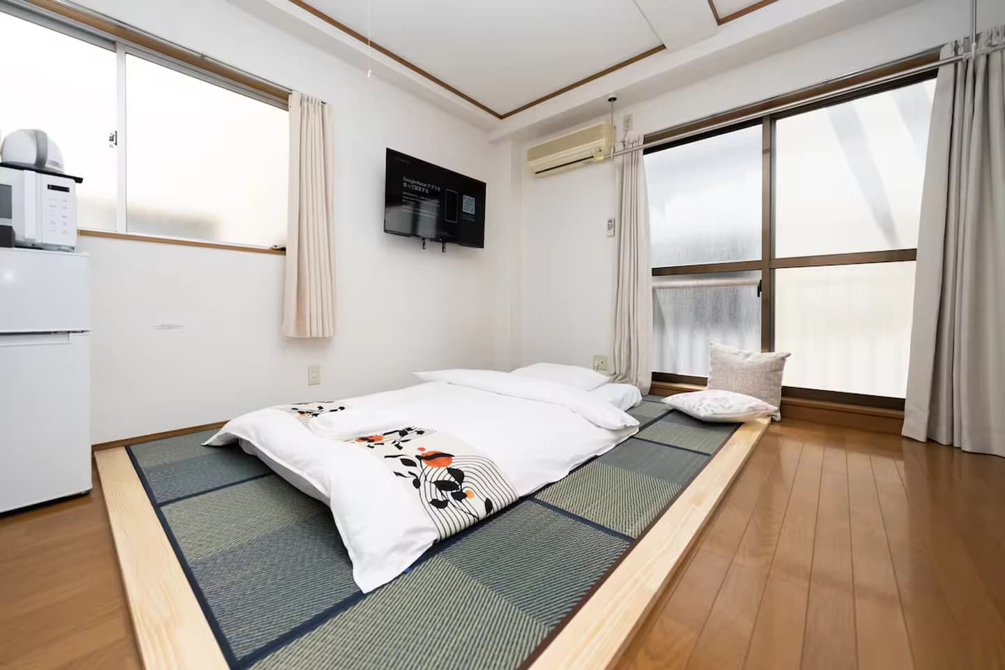 Japanese futon bed on a raised tatami mat platform in a bright bedroom with large windows.